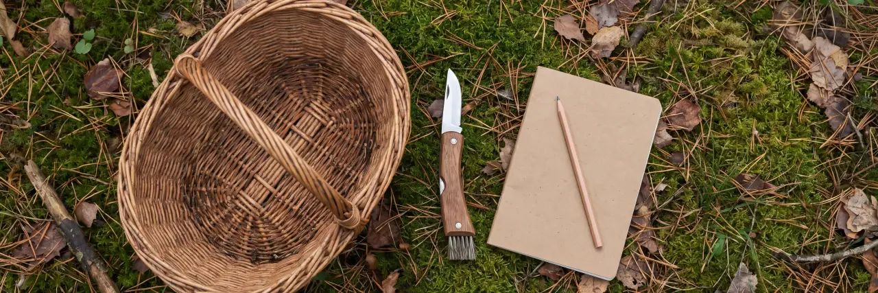 Cesta de mimbre, navaja con cepillo y libreta sobre el musgo